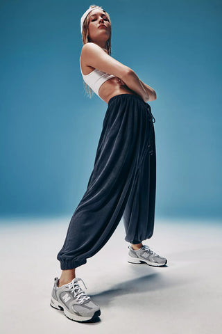 Person wearing a white sports bra and dark jogger pants with gray sneakers against a blue background