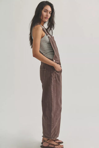 Woman wearing brown overalls and a green tank top on a plain background