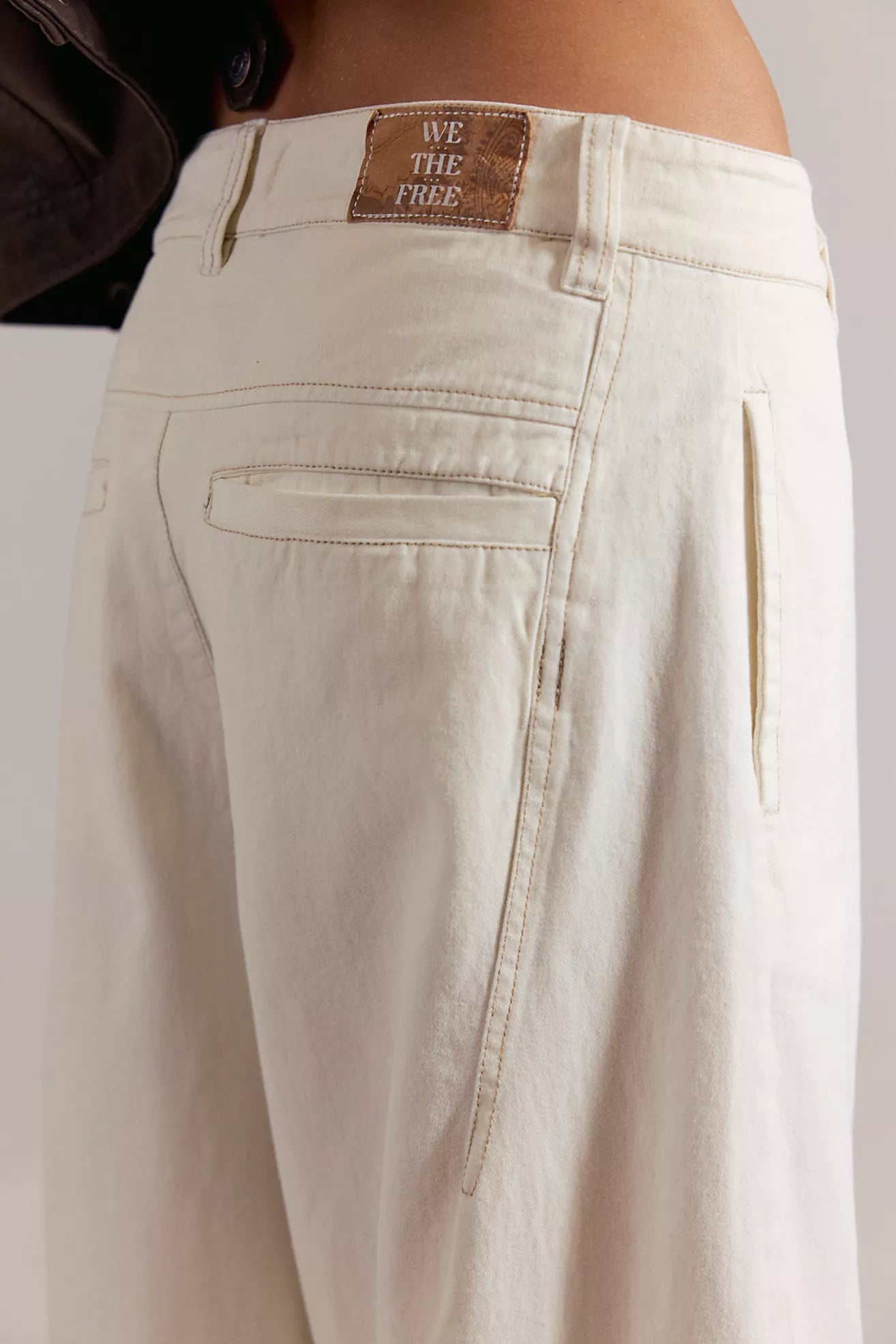 Close-up of beige pants with a brand label on a plain background