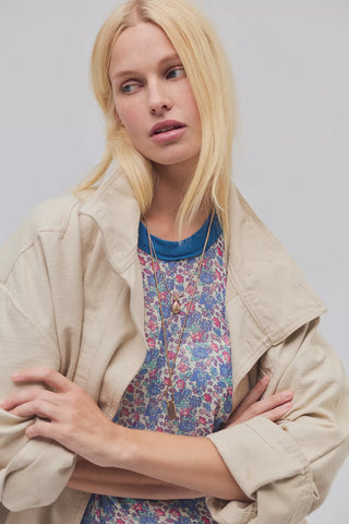 Woman wearing a beige jacket over a floral dress with a neutral background