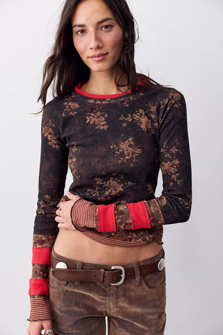 A woman modeling a long-sleeve cropped knit top with a dark brown and black floral pattern, red ribbed collar and cuff accents, and brown corduroy pants against a light gray background.