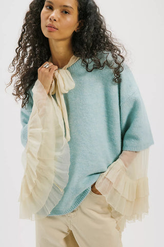 Woman wearing a light blue poncho with beige accents on a white background