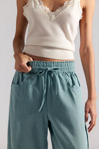 Person wearing a white lace-trimmed top and teal striped pants on a plain background