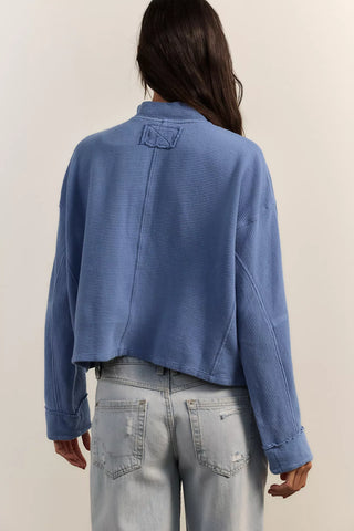 Person wearing a blue textured jacket and light gray jeans against a plain background