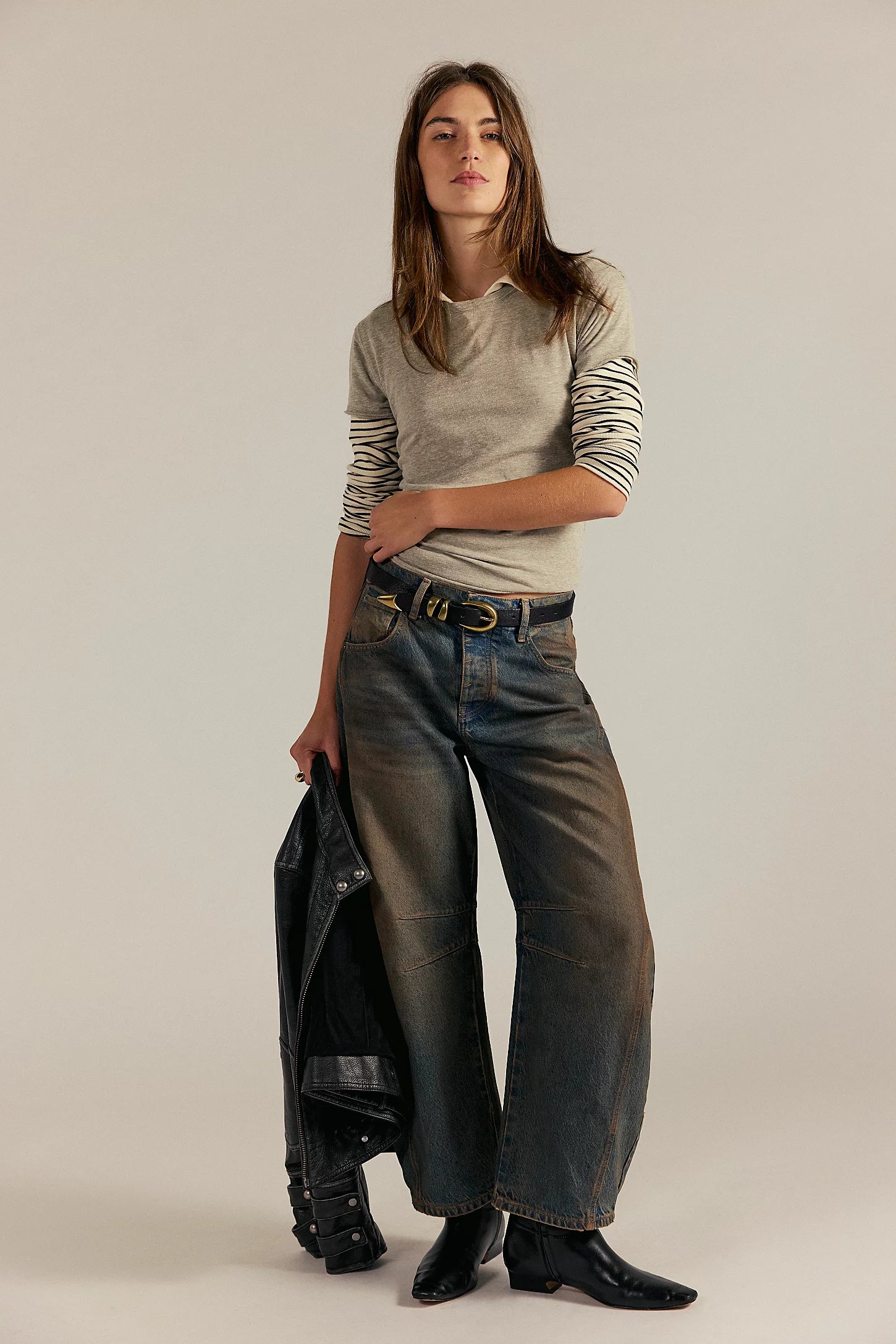 Woman wearing a striped shirt and jeans holding a black jacket against a plain background
