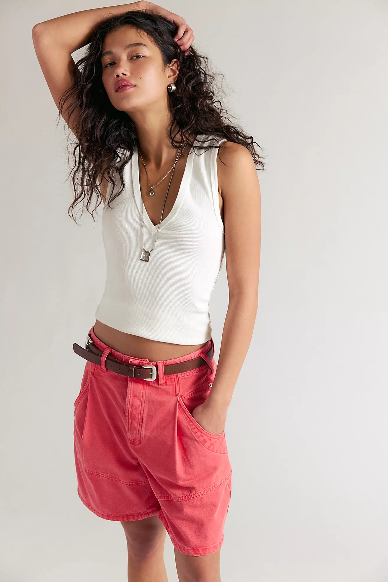Woman wearing a white sleeveless top and red shorts against a plain background