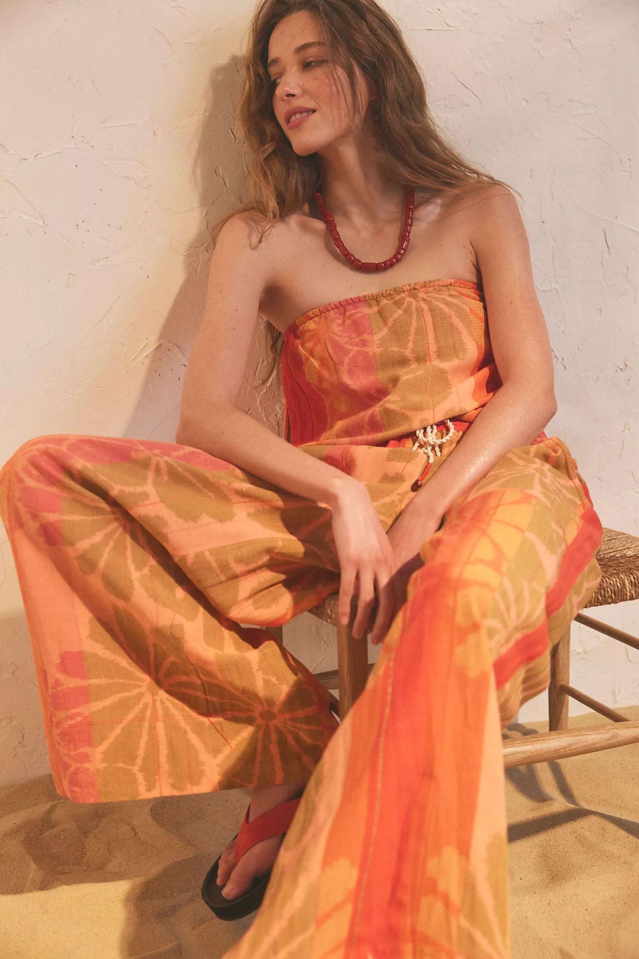 Woman wearing a colorful dress sitting on a chair against a white wall.