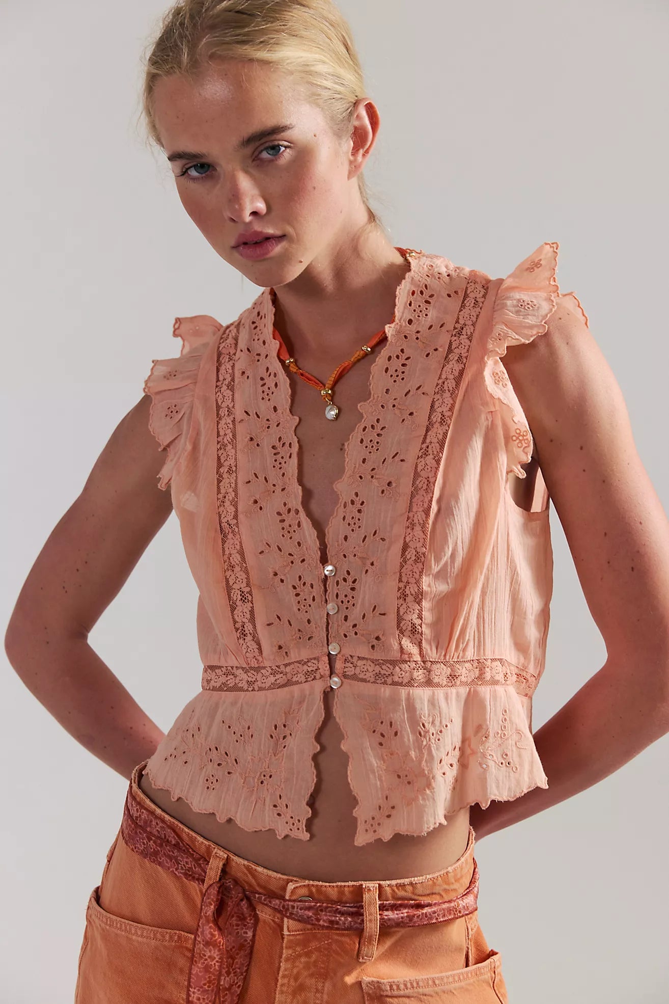 Woman wearing a light pink sleeveless top with lace details on a plain background