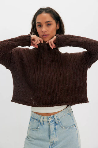 Woman wearing a brown sweater and light blue jeans on a white background