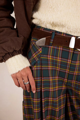Person wearing a plaid skirt with a brown jacket and white sweater.
