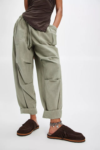Person wearing olive green cargo pants and brown shoes on a white background