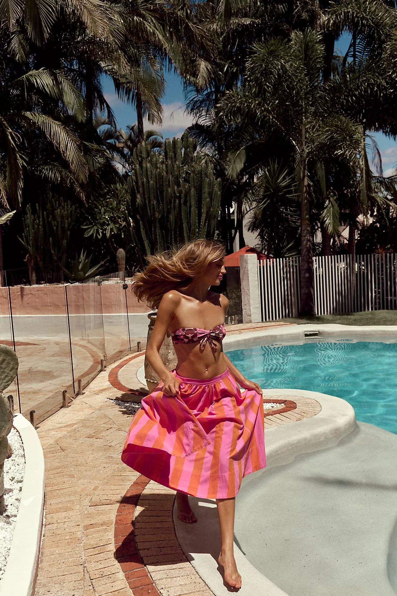 Woman in a pink dress by a pool with palm trees in the background