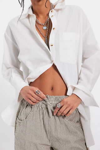 Person wearing a white button-up shirt and striped pants with jewelry.
