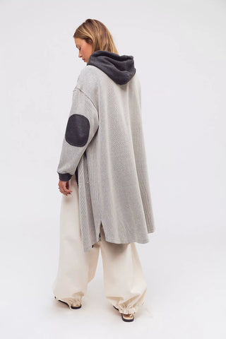 Person wearing a long gray cardigan with black elbow patches on a white background