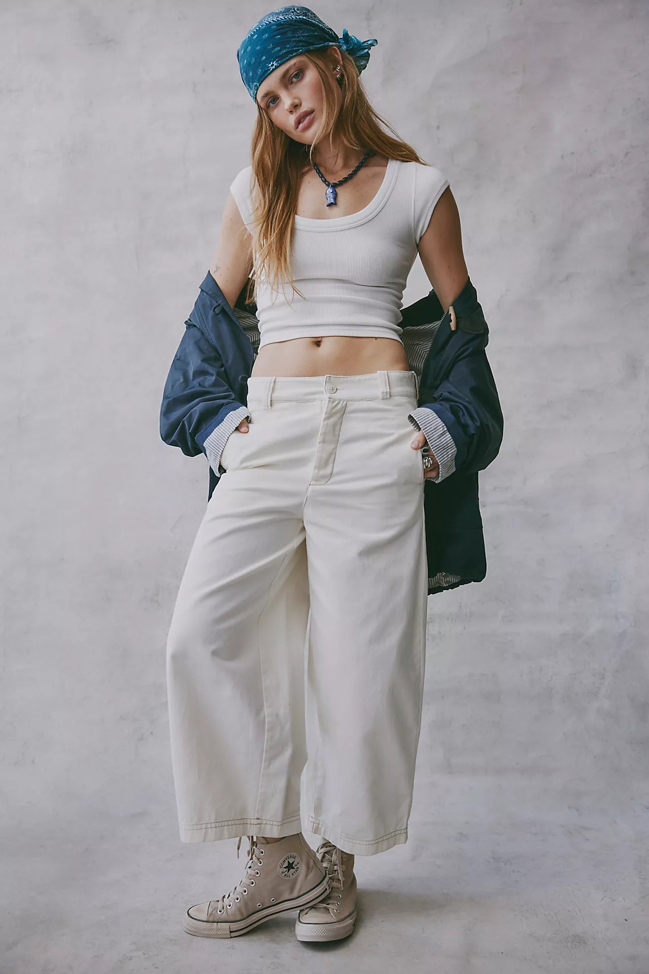 Person wearing a white crop top, beige pants, and a blue bandana against a gray background
