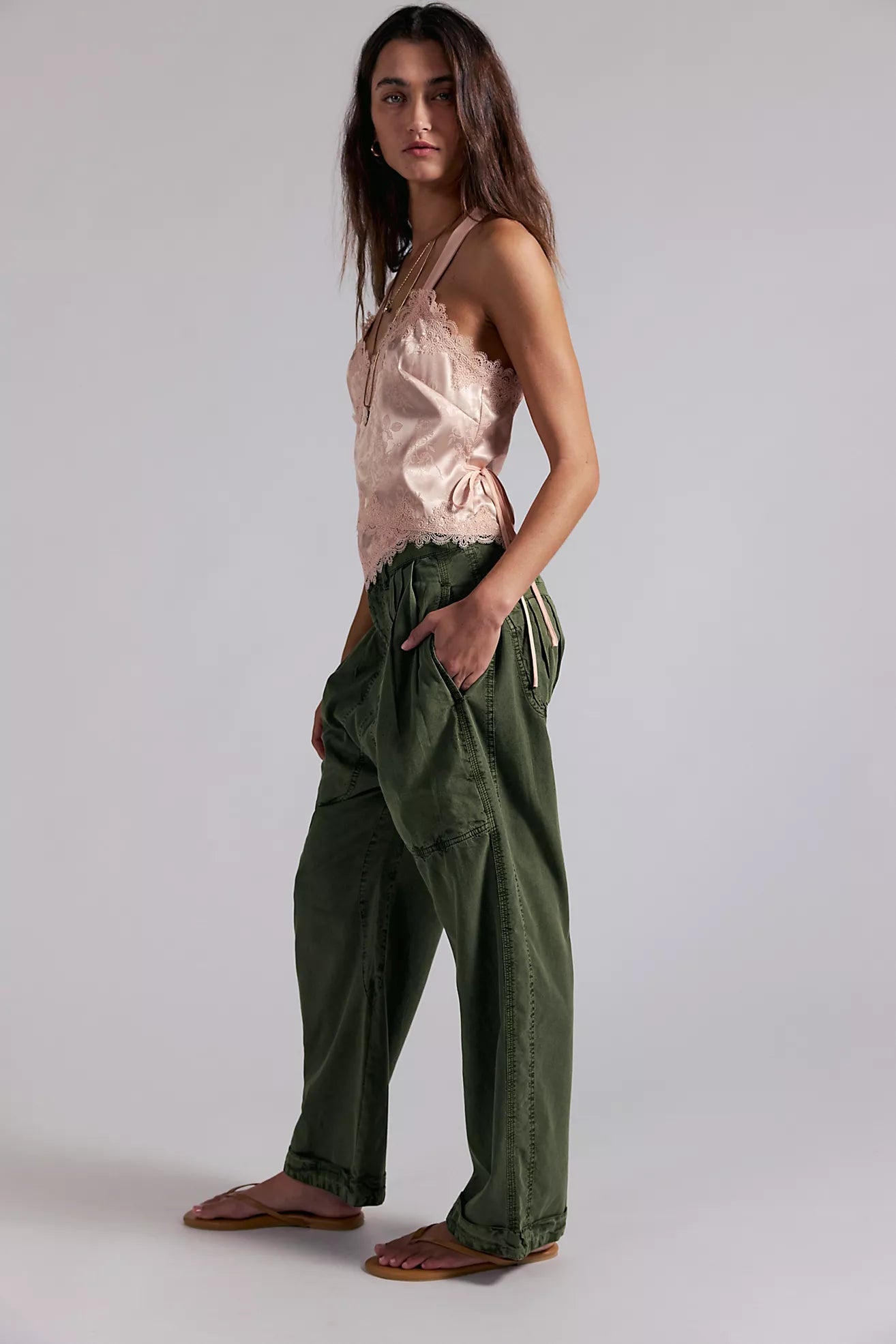 Woman wearing a pink top and green pants on a plain background