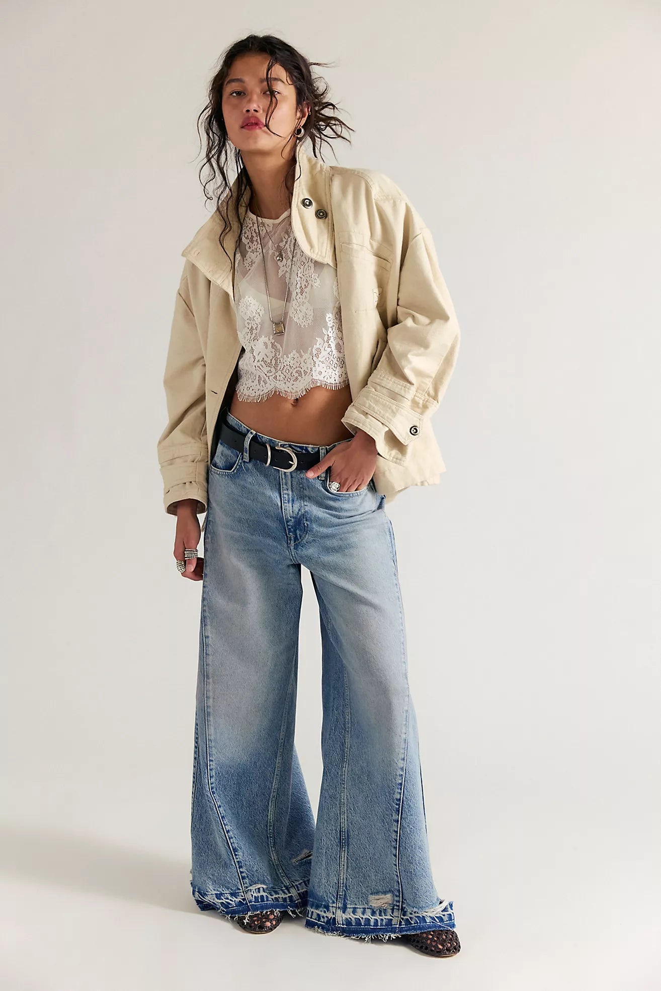 Person wearing a beige jacket, lace top, and wide-leg jeans on a white background