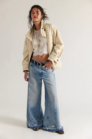 Person wearing a beige jacket, lace top, and wide-leg jeans on a white background