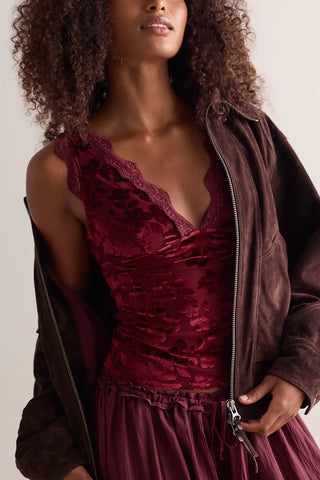 A close-up of a model wearing a deep burgundy velvet lace bodice top with a ruffled neckline, layered under a dark brown suede zip-up jacket.