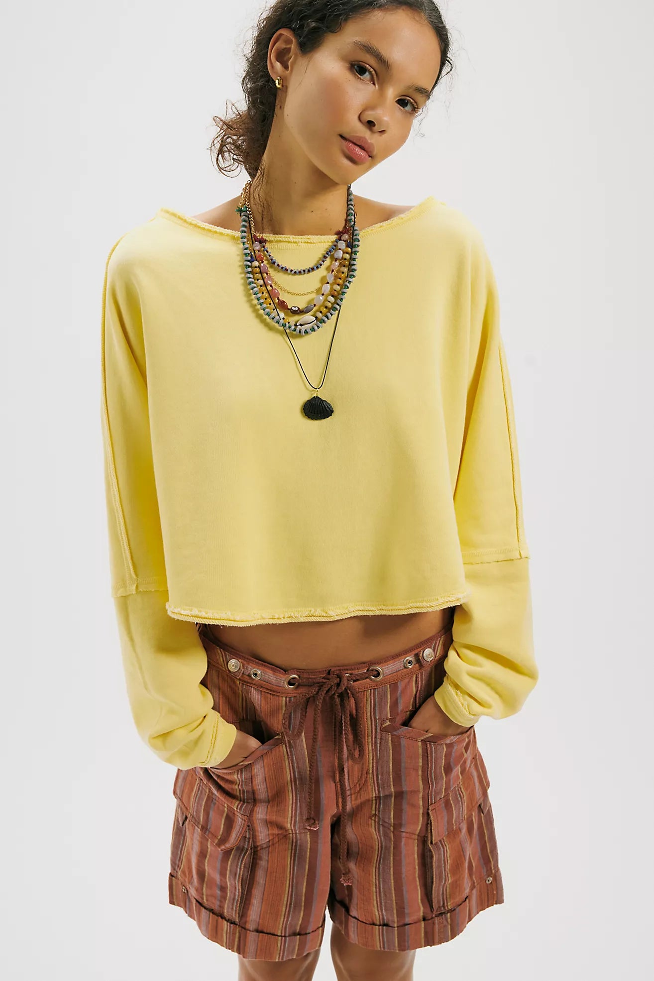 Woman wearing a yellow cropped sweatshirt and plaid shorts on a white background