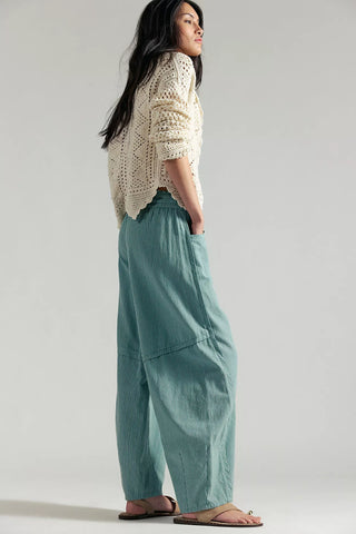 Woman wearing a cream sweater and teal pants on a plain background