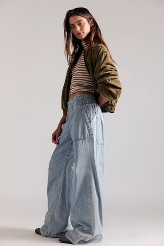 Woman wearing a green jacket, striped shirt, and light blue jeans on a plain background