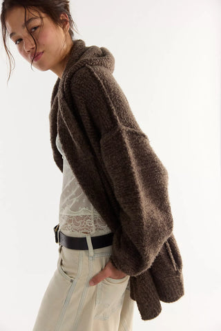 Women wearing a brown knit cardigan and cream jeans in front of a neutral photo background.