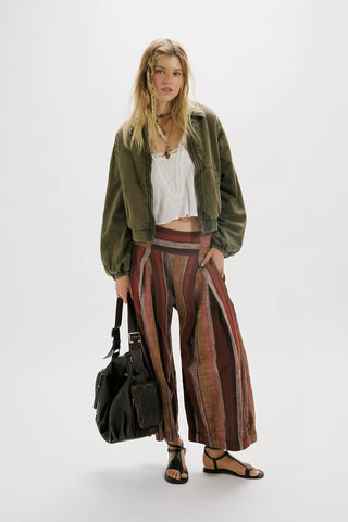 Woman wearing a green jacket, white top, and striped pants holding a black bag on a white background