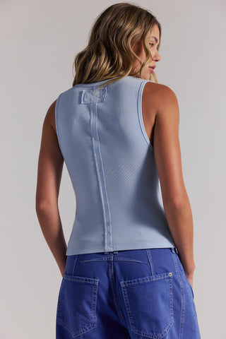 Woman wearing a light blue sleeveless top and blue pants on a plain background