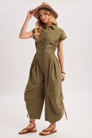 Woman wearing an olive green jumpsuit and hat on a white background