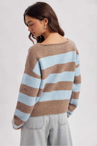 A woman wearing a brown and light blue striped knit sweater, shown from a side-back angle against a plain light gray studio background.