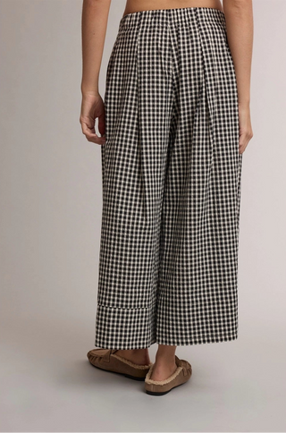 A person wearing black and white gingham cropped wide-leg pants with brown flat shoes, shown from the waist down against a plain light gray studio background.