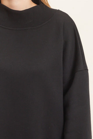 Close-up of a person wearing a black crewneck sweatshirt, showing the ribbed collar and sleeve seam against a plain light background.