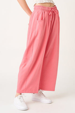 A person wearing wide-leg pink drawstring pants with side pockets, paired with white sneakers, shown against a plain light background.