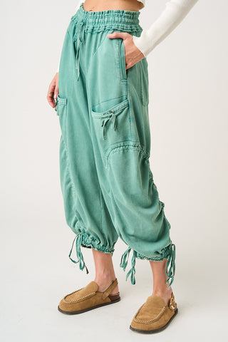 Person wearing teal baggy pants with tassels on a white background