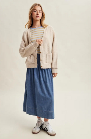 Woman wearing a beige cardigan, striped shirt, and blue skirt on a plain background
