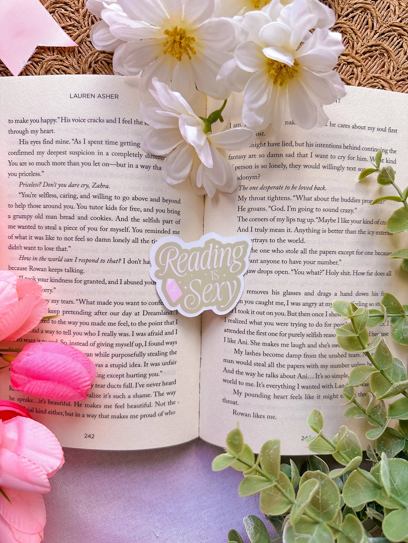 Open book with flowers and a decorative stick saying reading is sexy on a textured surface