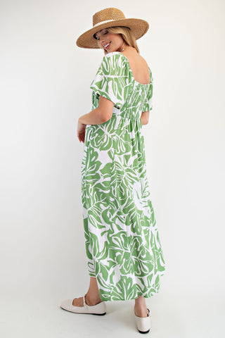 Woman wearing a green and white leaf-patterned dress with a straw hat on a white background