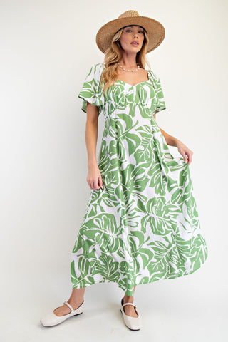 Woman wearing a green and white leaf-patterned dress with a straw hat on a white background