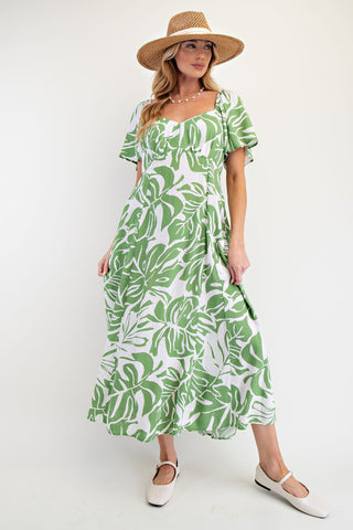 Woman wearing a green leaf-patterned dress and straw hat on a white background