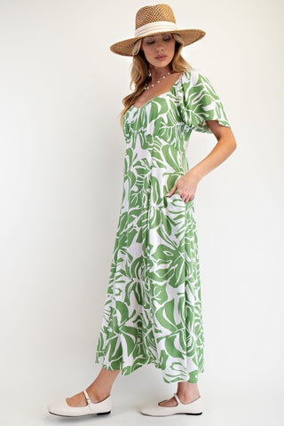 Woman wearing a green and white leaf-patterned dress with a straw hat on a white background