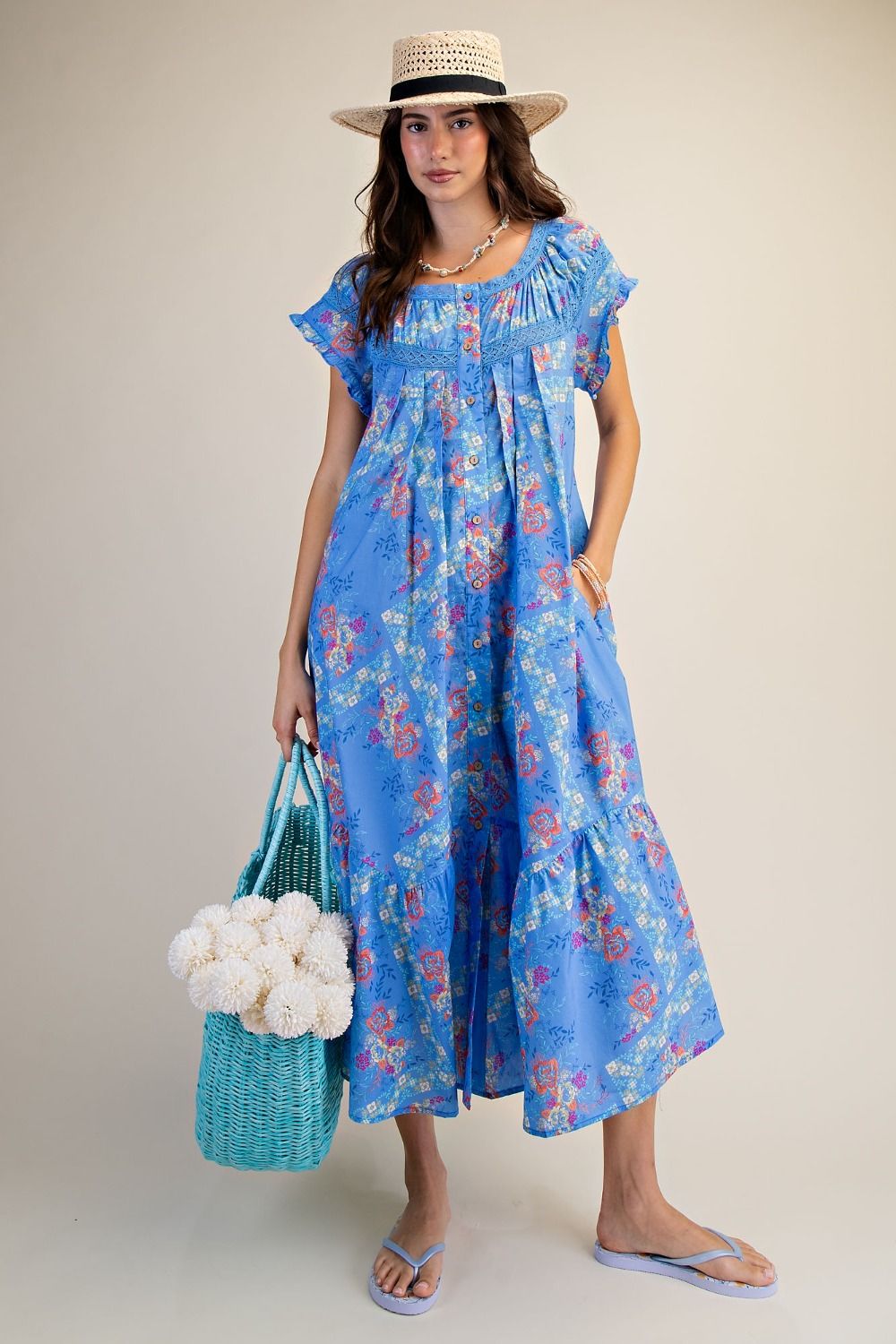 Woman wearing a blue floral dress holding a bag with white flowers against a plain background