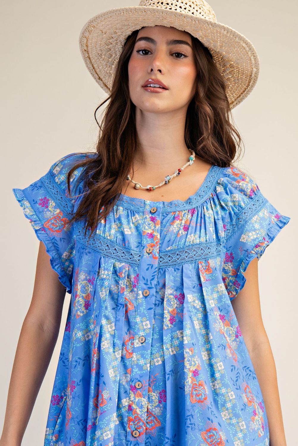 Woman wearing a blue floral dress and straw hat against a neutral background