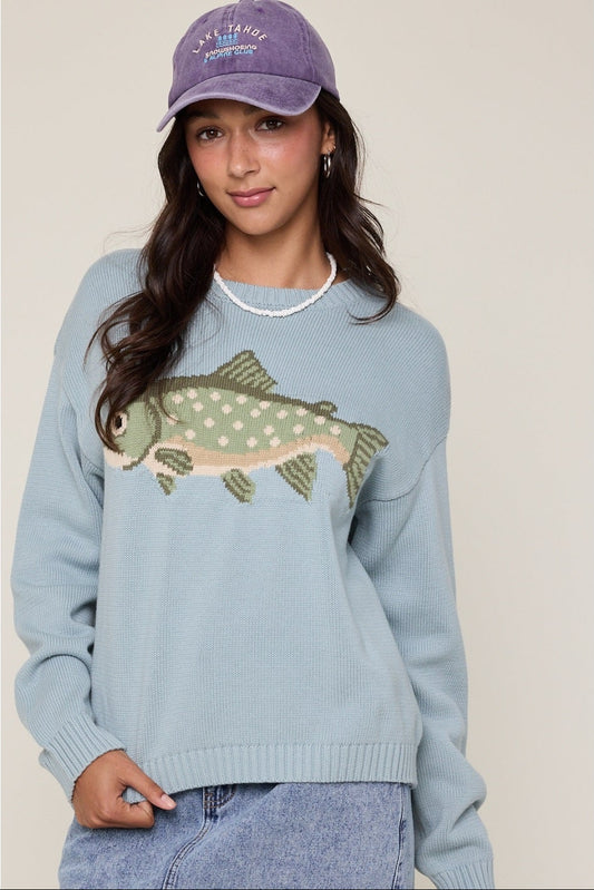 Woman wearing a light blue sweater with a fish design and a matching cap.