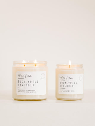 Two candles with white labels reading 'Eucalyptus Lavender', one with a single wick in a smaller jar and one with a double wick in a larger jar, set against a neutral background.