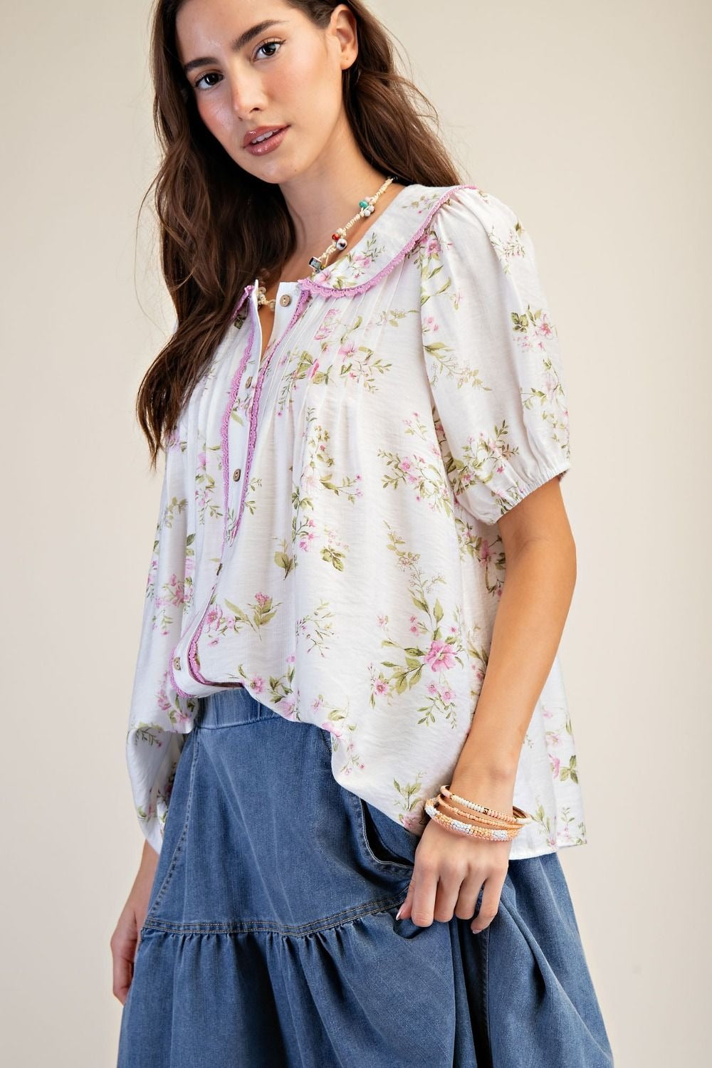 Woman wearing a floral blouse and denim skirt against a plain background