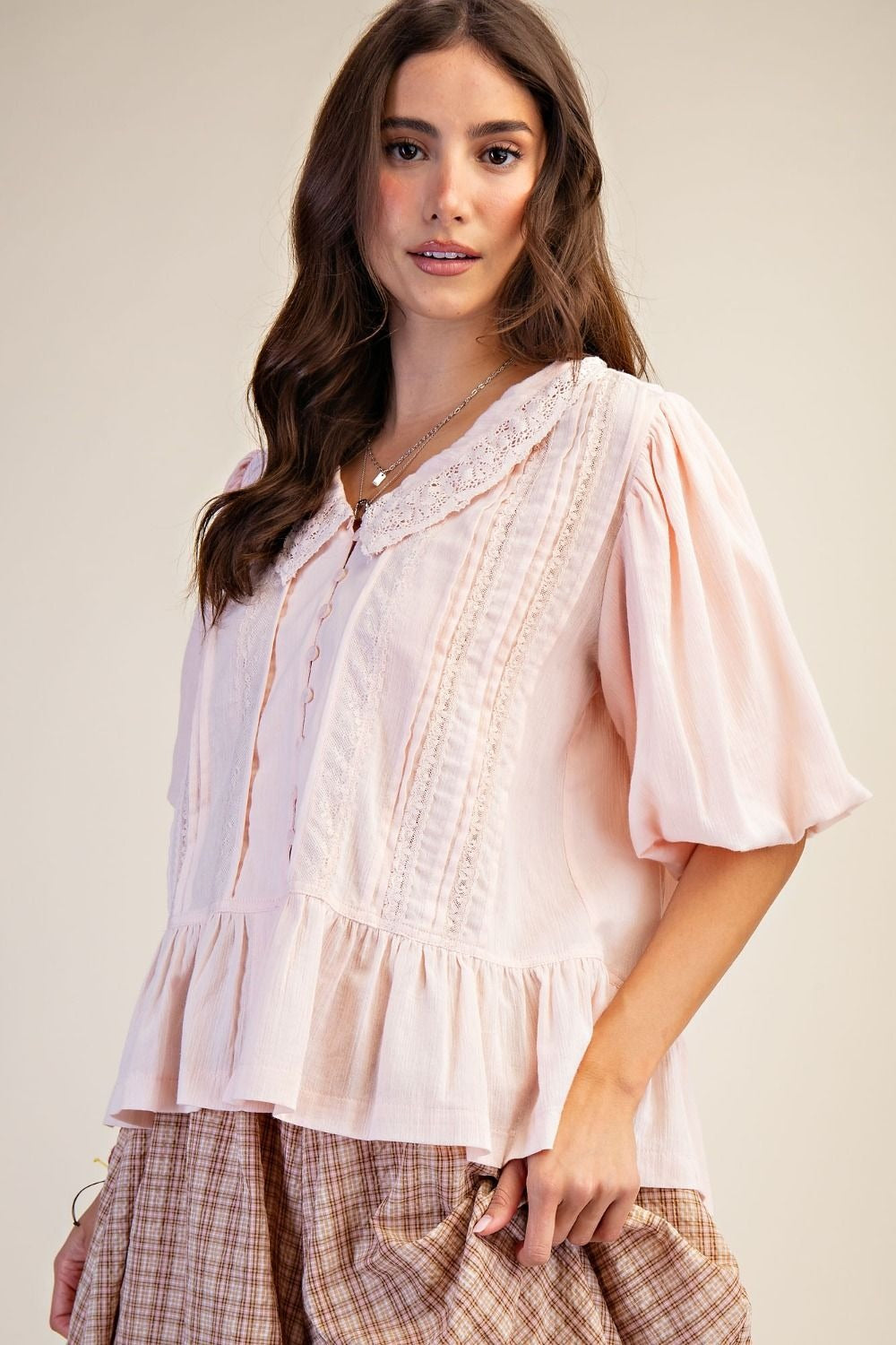 Woman wearing a light pink blouse with lace details on a plain background