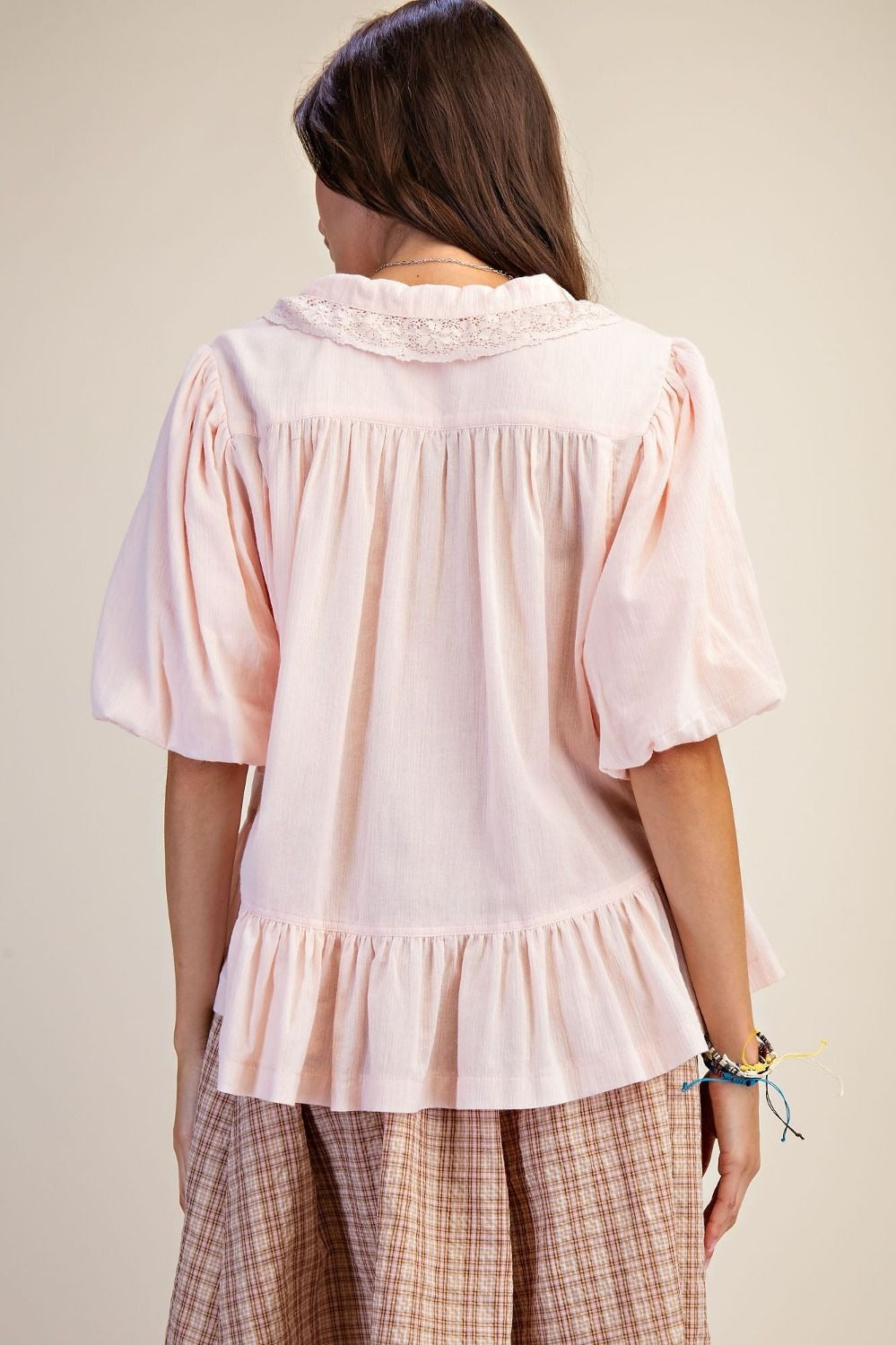 Woman wearing a light pink blouse with ruffled details on a plain background