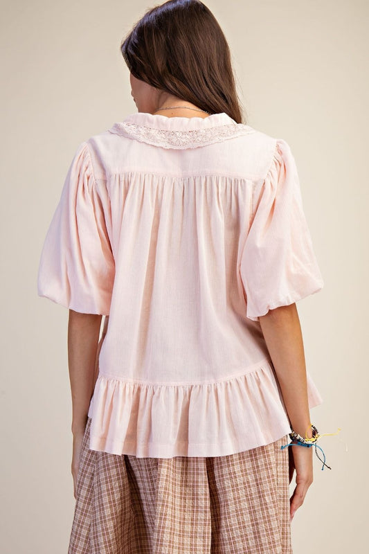 Woman wearing a light pink blouse with ruffled details on a plain background