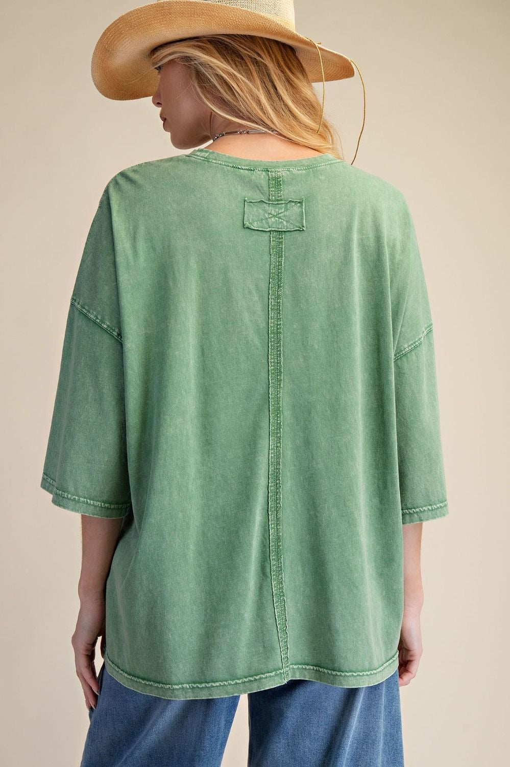 Person wearing a green oversized shirt and blue jeans with a beige background